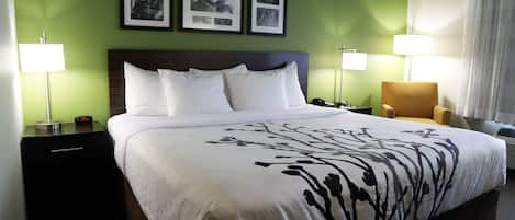 A hotel room with a large bed, two bedside tables, a chair, and a wall with three framed pictures.