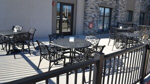 Terrasse extérieure avec des tables et des chaises en métal, un bâtiment en pierre en arrière-plan et une rambarde en métal.