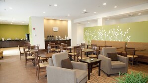 Un hall d’hôtel comprenant des espaces aménagés avec des sièges, un comptoir d’accueil et un coin café.