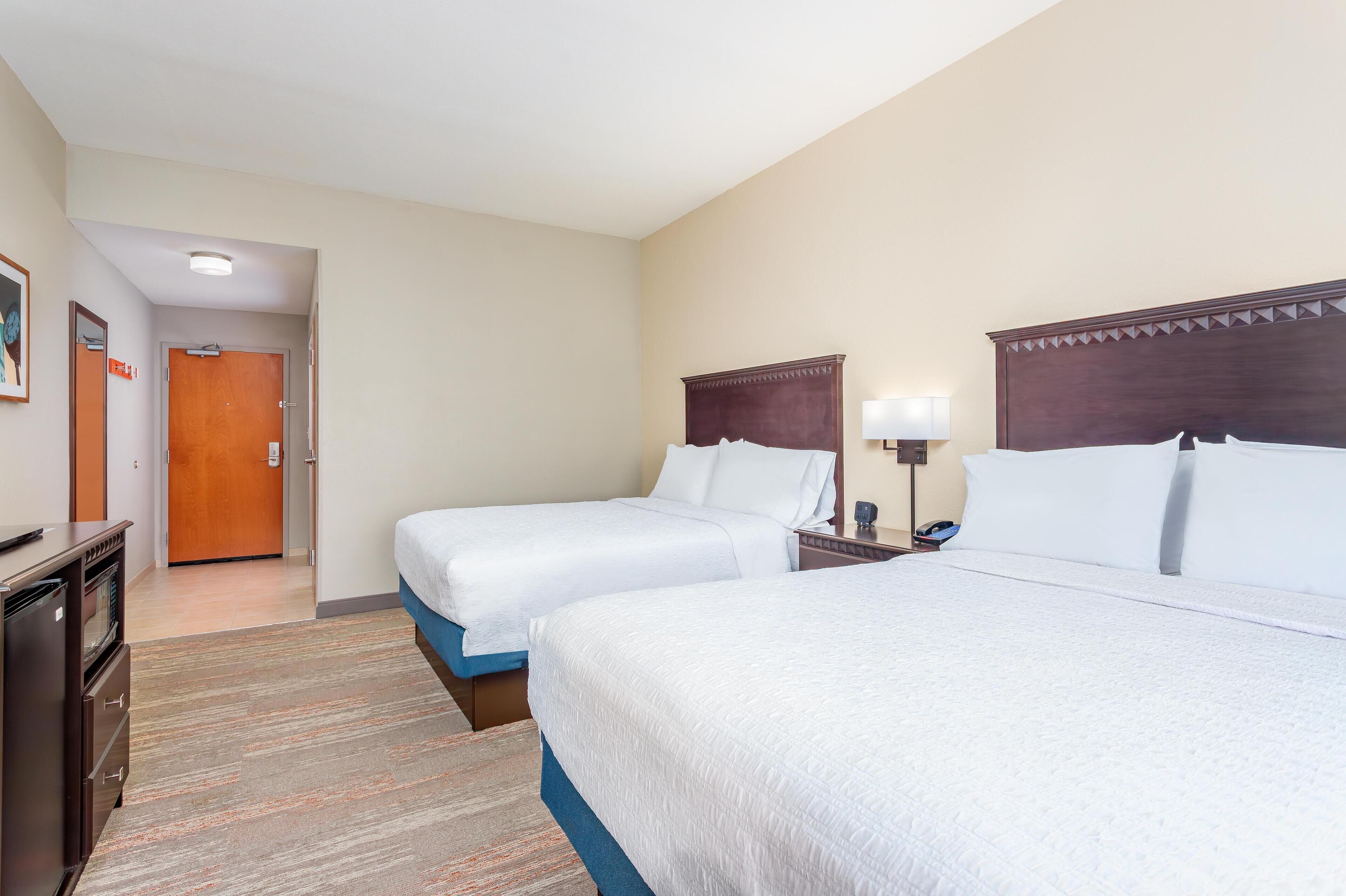 A hotel room with two beds, a desk, and a door leading to a hallway.