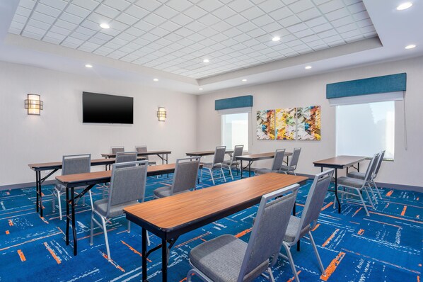 Un salón de conferencias con una mesa grande, varias sillas, un televisor de pantalla plana y obras de arte en la pared.