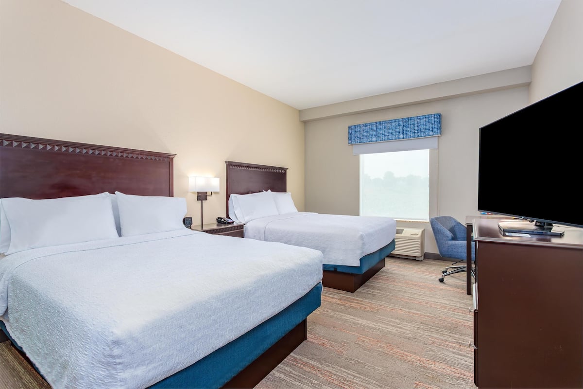 A hotel room with two beds, a desk, a TV, and a window with a view.