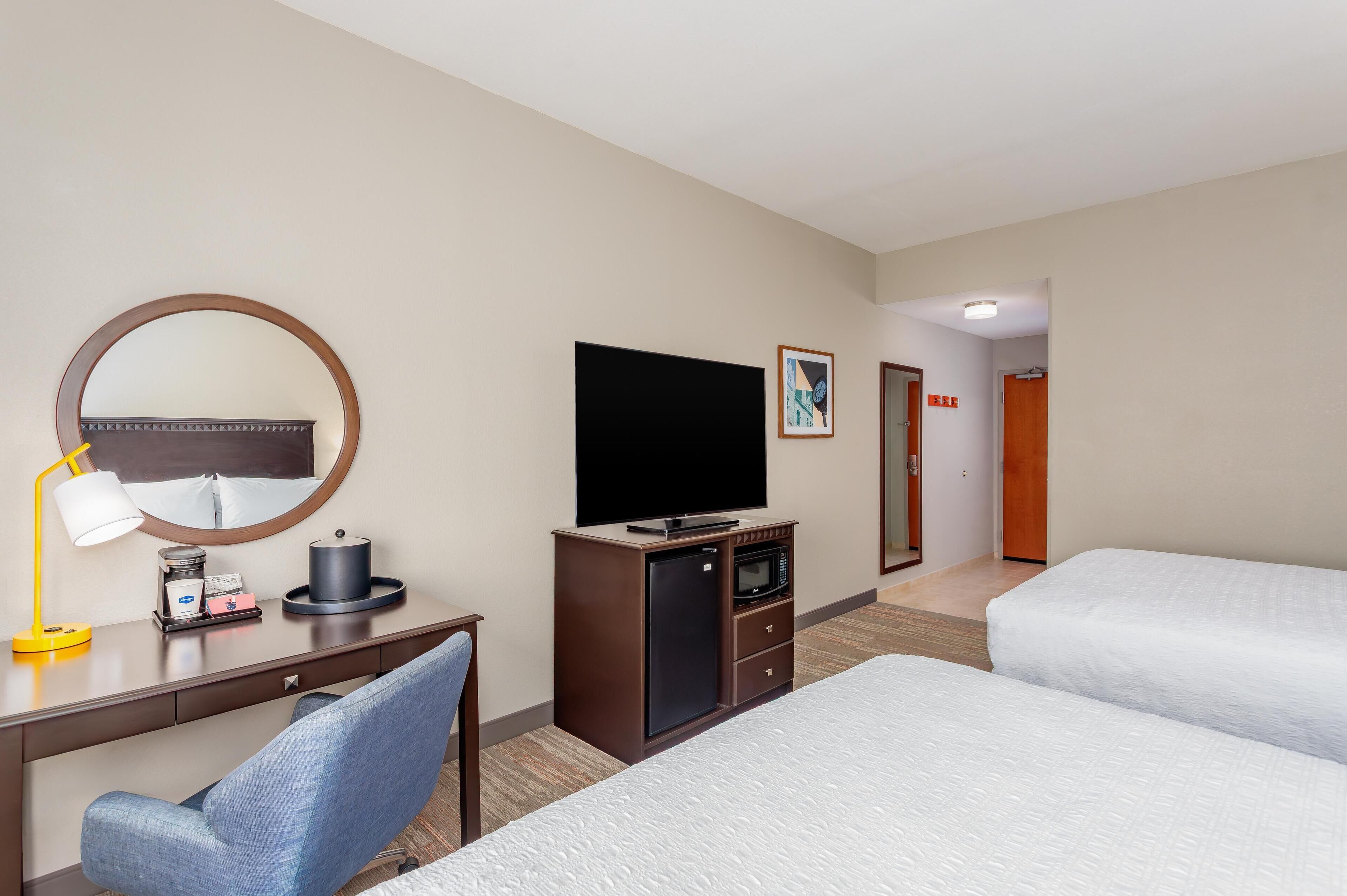 A hotel room with a desk, a television, a microwave, a refrigerator, and two beds.