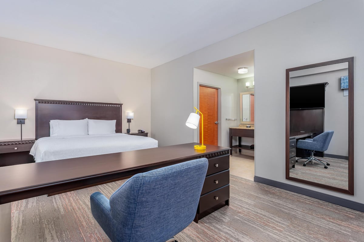 A hotel room with a bed, desk, chair, lamp, and a mirror.