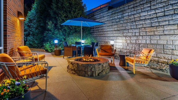 An outdoor patio with stone walls, a fire pit, and orange chairs. - Hampton Inn & Suites Parkersburg Downtown (Parkersburg)