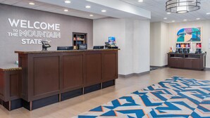 A hotel reception area with a 'Welcome to the Mountain State' sign, a reception desk, a minibar, and a coffee station. - Hampton Inn & Suites Parkersburg Downtown (Parkersburg)