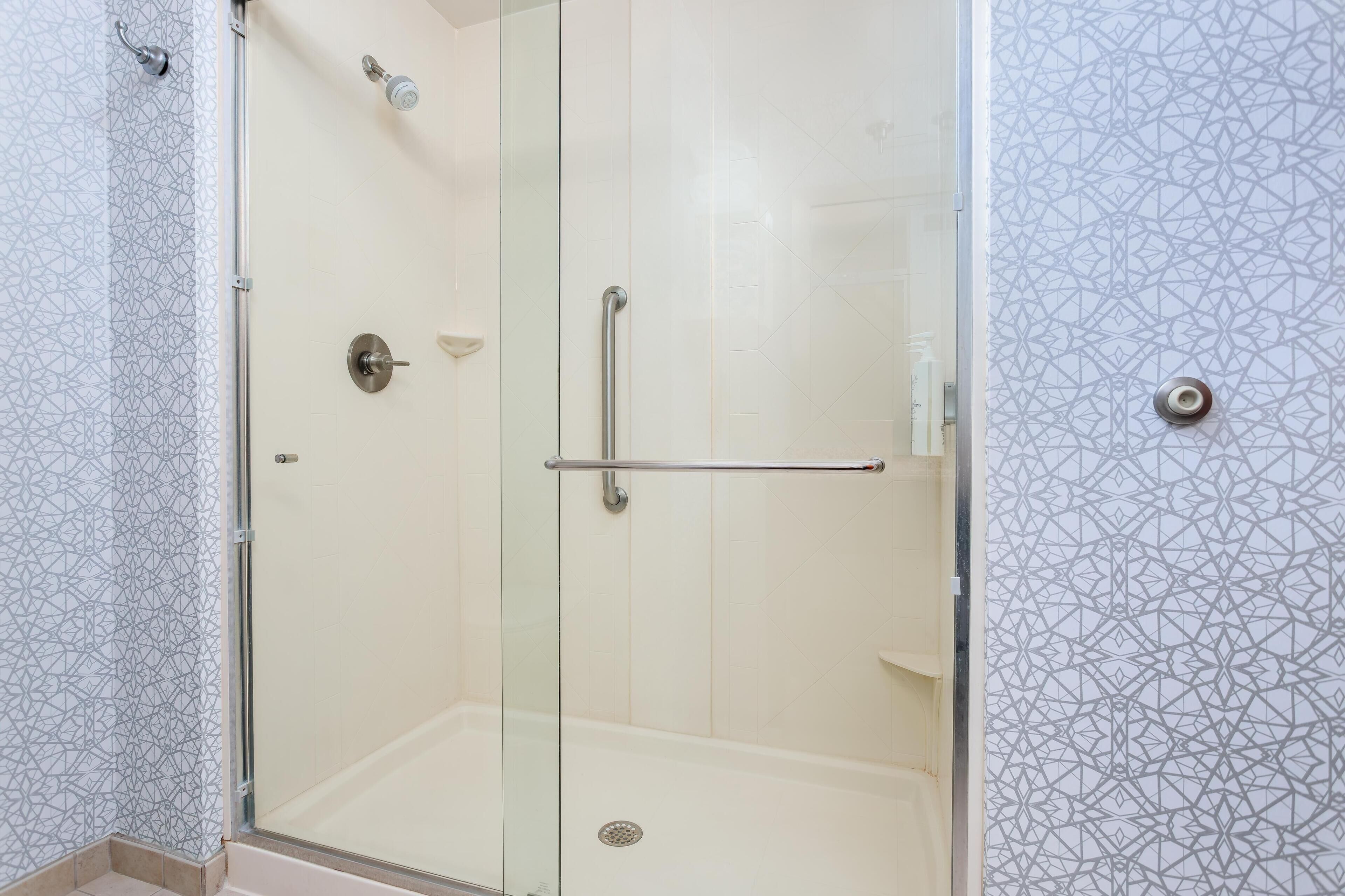 Un espace douche clos par des parois de verre, doté d’une porte en verre, d’une barre d’appui et d’un pommeau de douche.