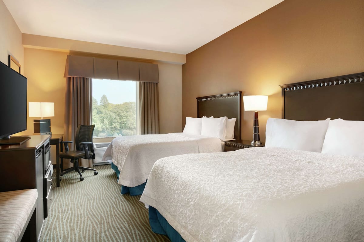 A hotel room with two beds, a desk with a TV, a chair, and a window with curtains.