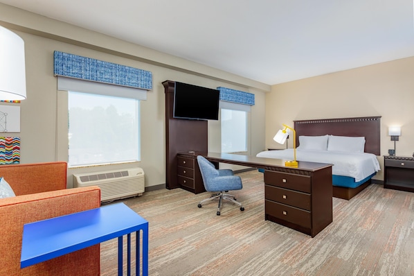 A hotel room with a desk, chair, bed, and a large window.