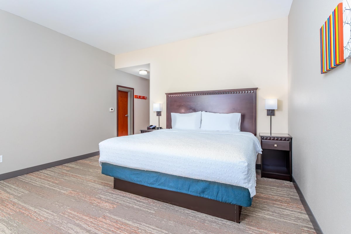 A hotel room with a large bed, a nightstand, a lamp, and a door.