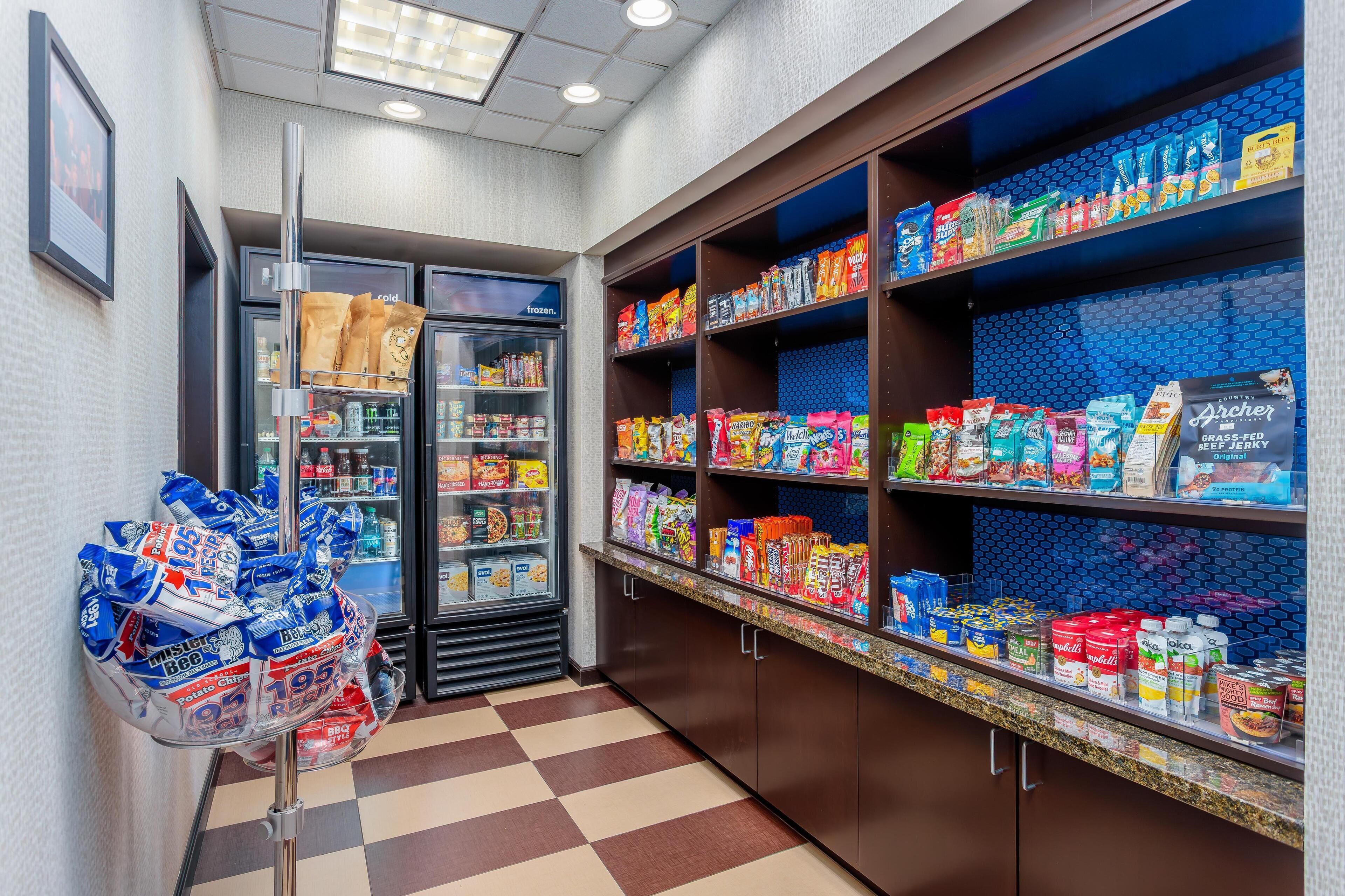 A snack bar with a variety of packaged foods and beverages, a refrigerated display case, and a checkered floor.