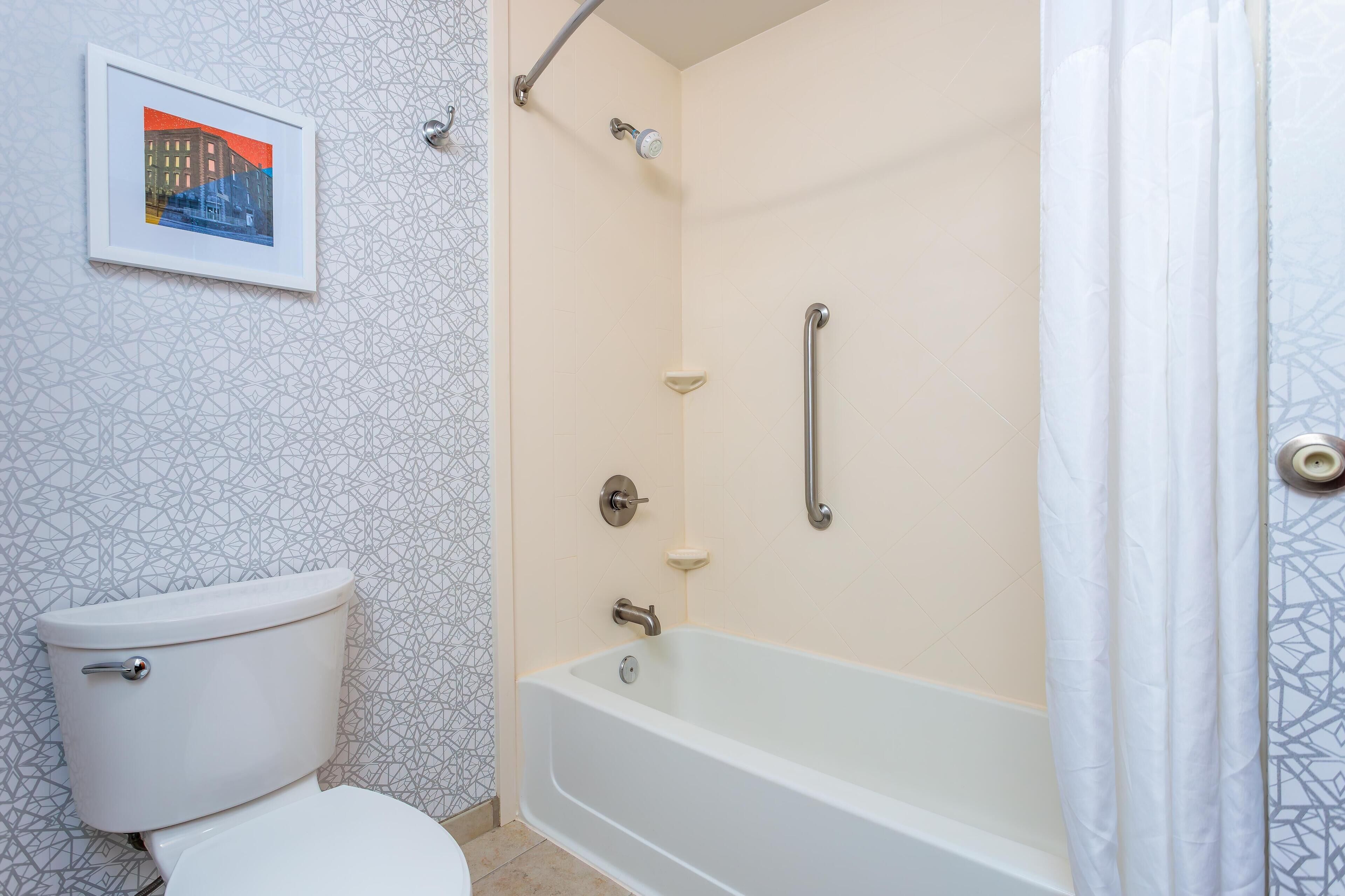 A bathroom with a toilet, a shower with a handrail, and a bathtub.