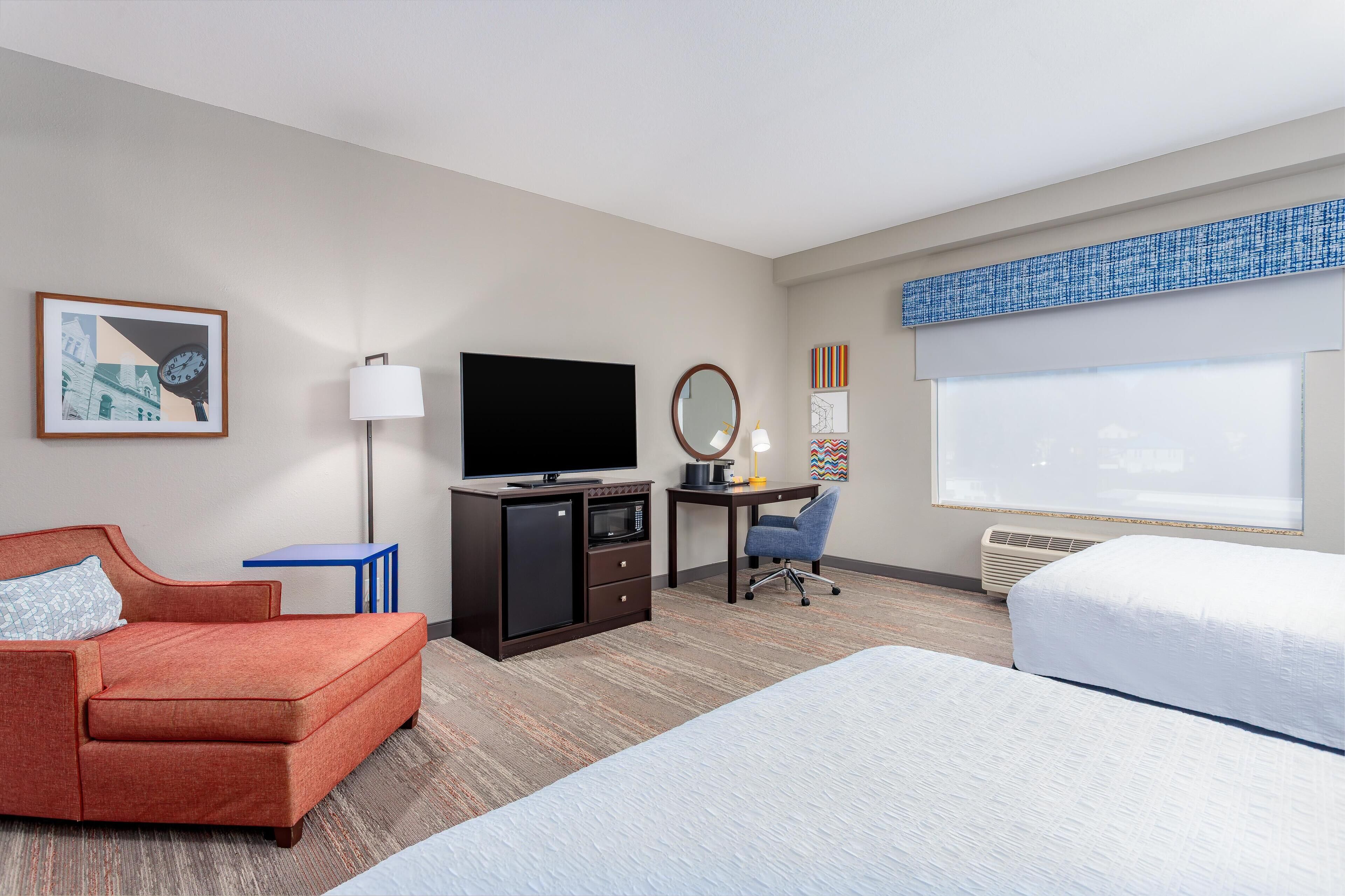 A hotel room with a bed, a desk, a television, a microwave, and a small table.