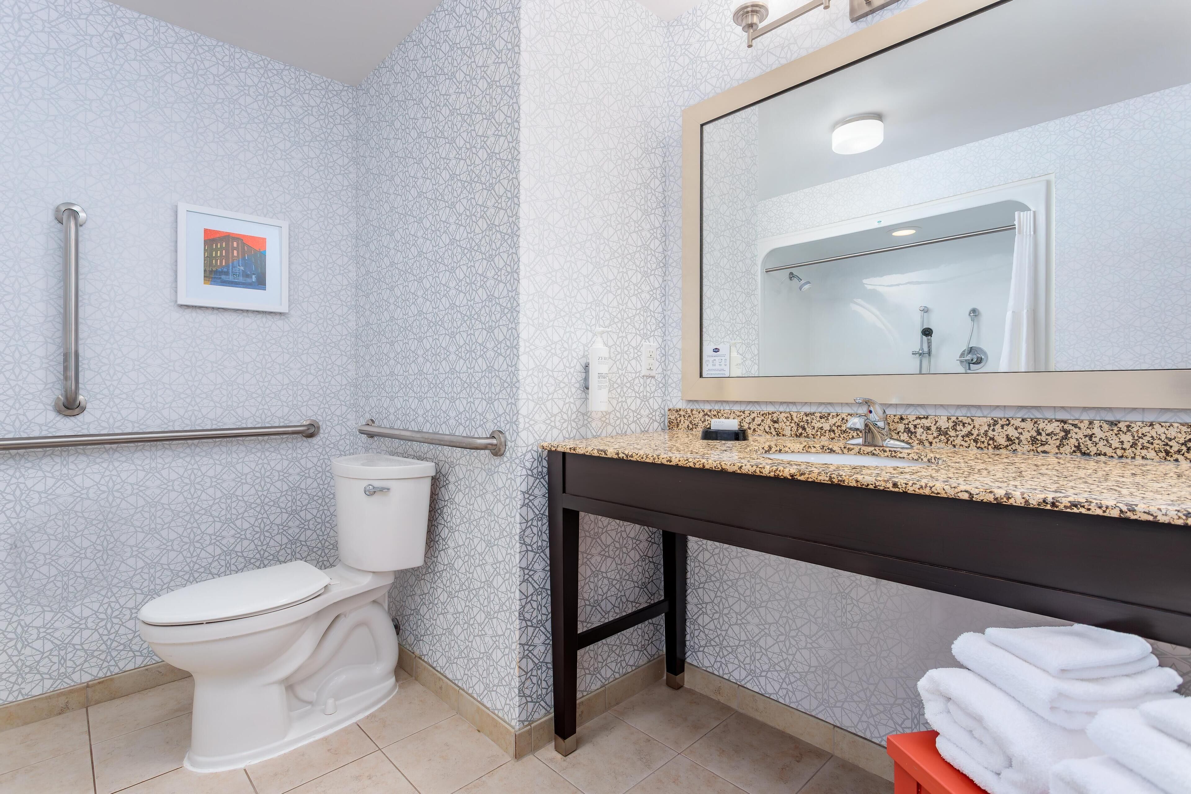 Un baño con inodoro, lavamanos con encimera de granito, espejo y barra para toallas.