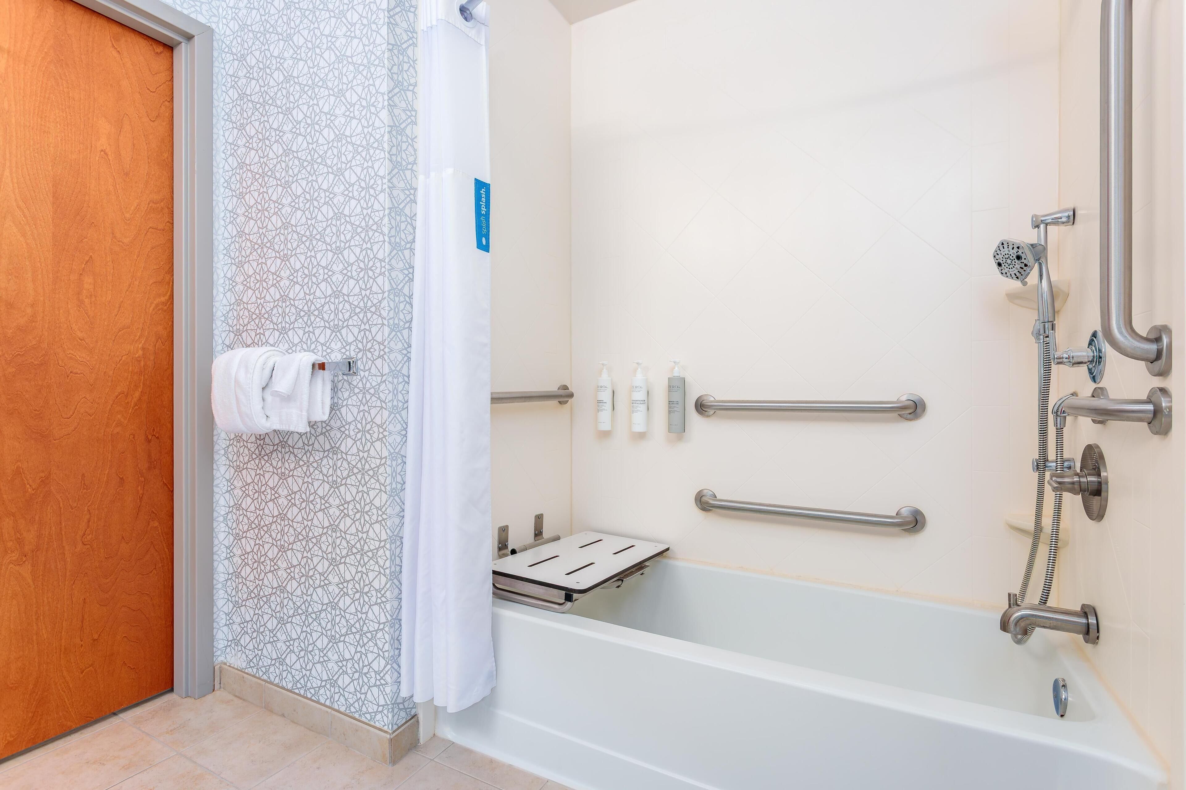 A modern bathroom with a bathtub, shower, and handrails.