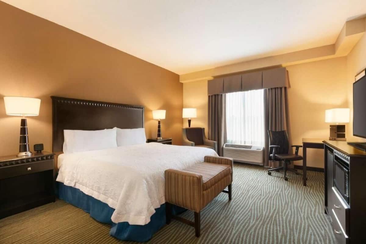 A hotel room with a large bed, two bedside tables, a desk, a chair, and a television.