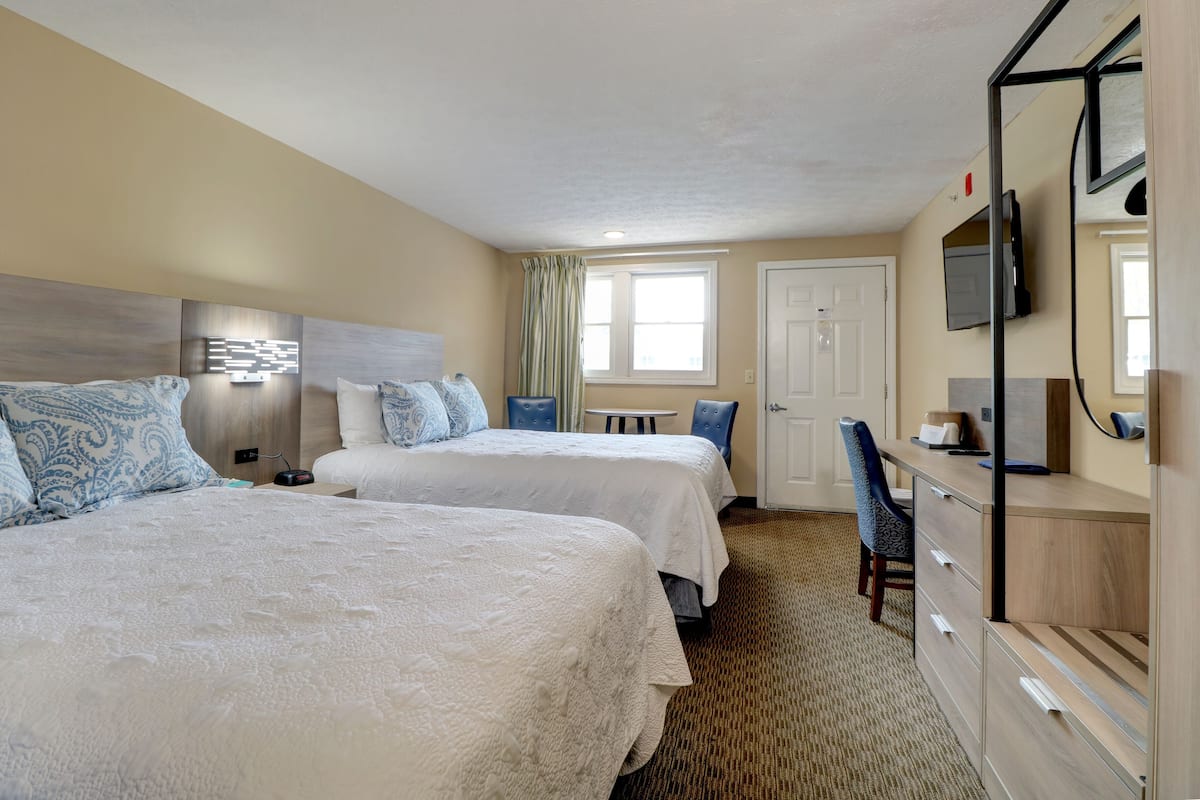 A hotel room with two beds, a desk, a chair, a TV, and a door.