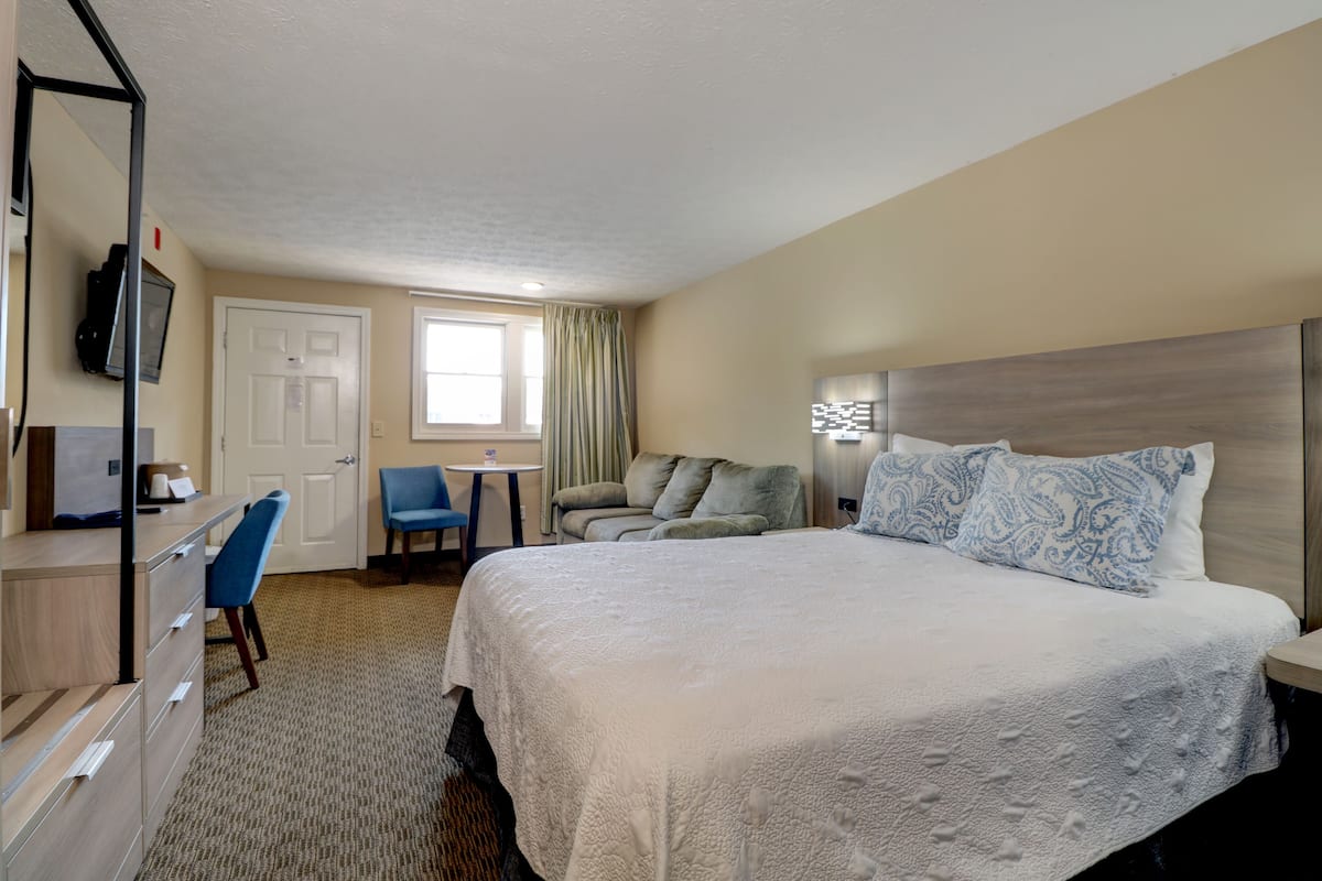 A hotel room with a large bed, a desk with a chair, a TV mounted on the wall, and a window with curtains.
