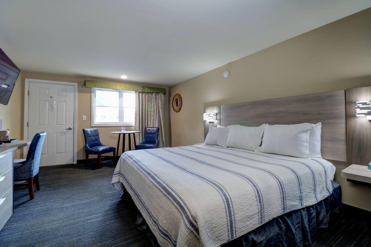 A hotel room with a large bed, a desk, two chairs, a small table, and a television.