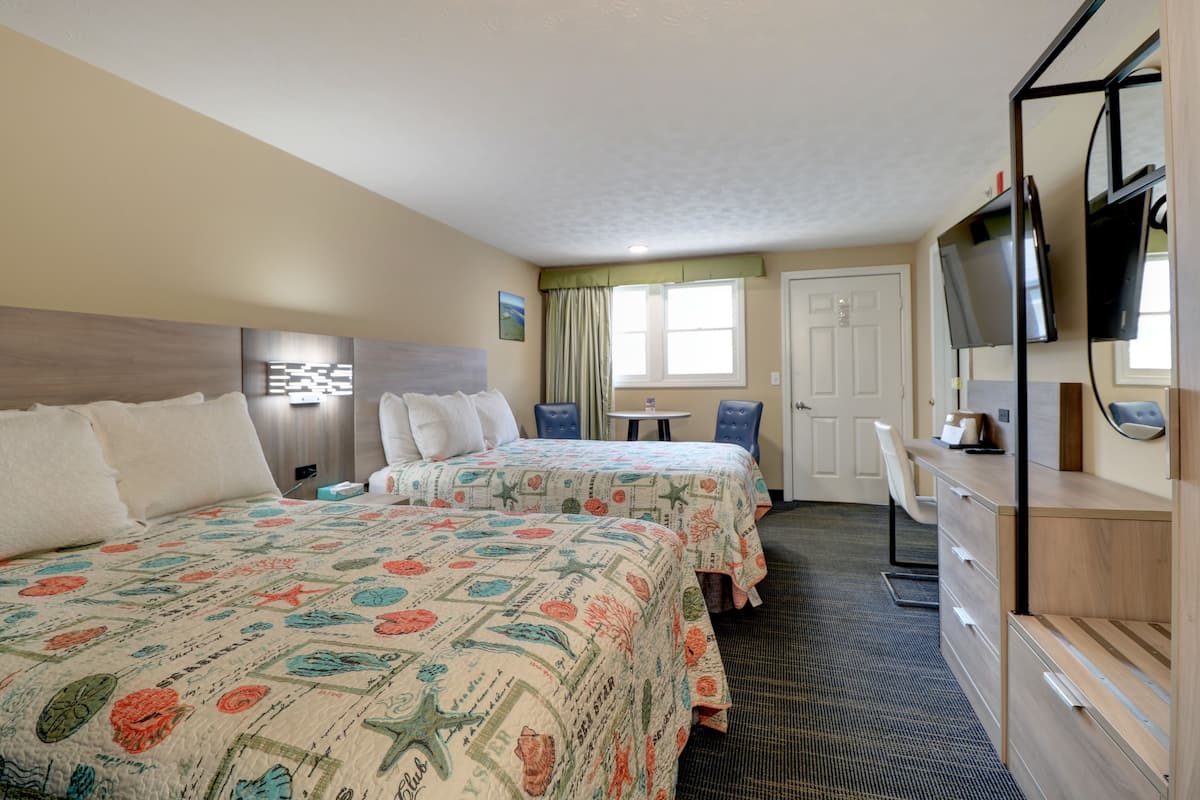 A hotel room with two beds, a desk, a TV, and a dresser.