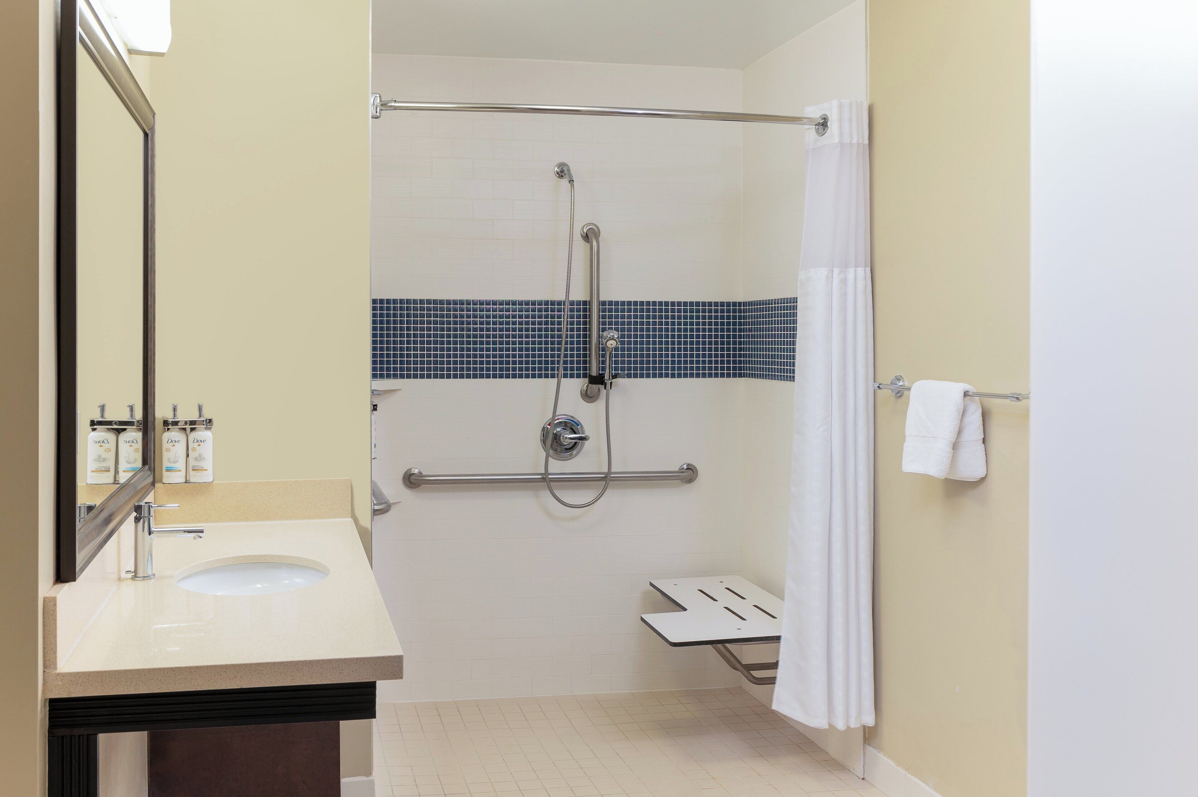 A bathroom with a sink, mirror, shower, and towel rack.