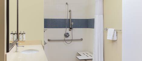 A bathroom with a sink, mirror, shower, and towel rack.