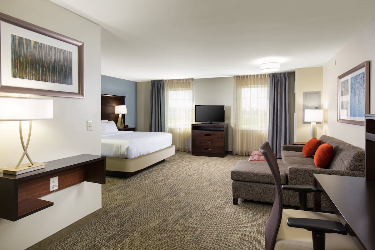 A hotel room with a bed, a desk with a chair, a television, and a sofa with cushions.