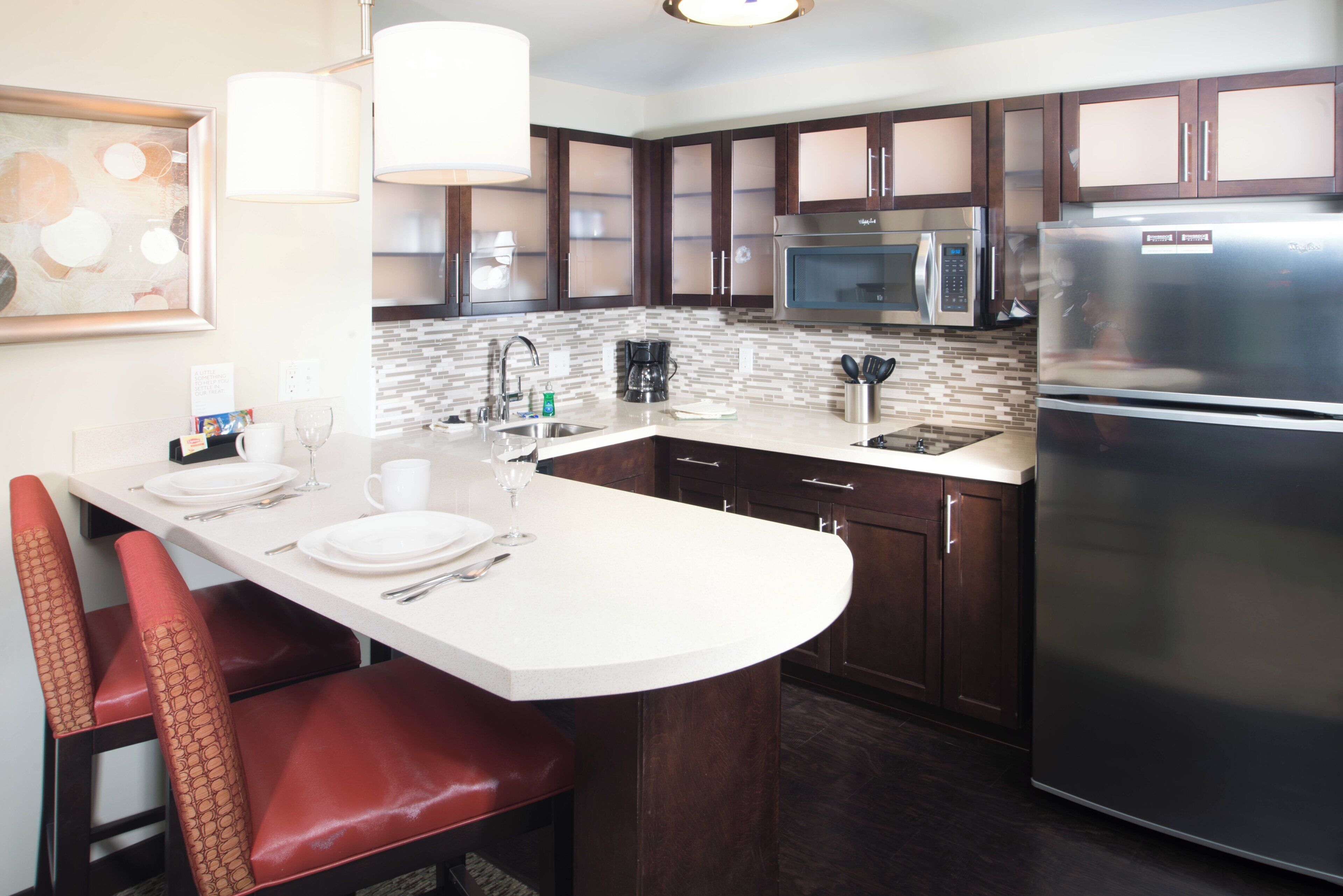 A modern kitchen with a central island, stainless steel appliances, and dark wooden cabinets.