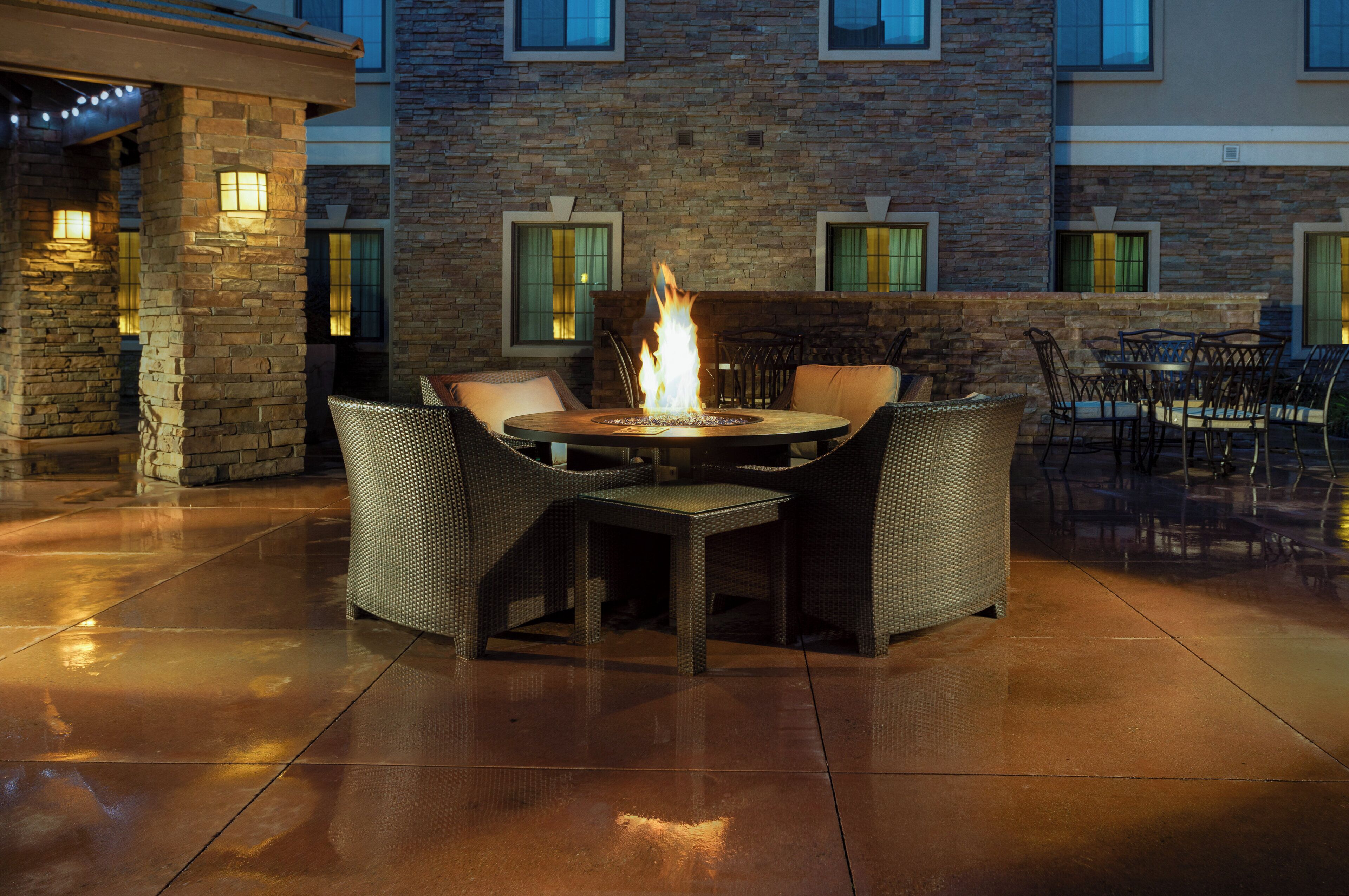 An outdoor patio area with a round table and chairs, a fire feature, and a stone wall.