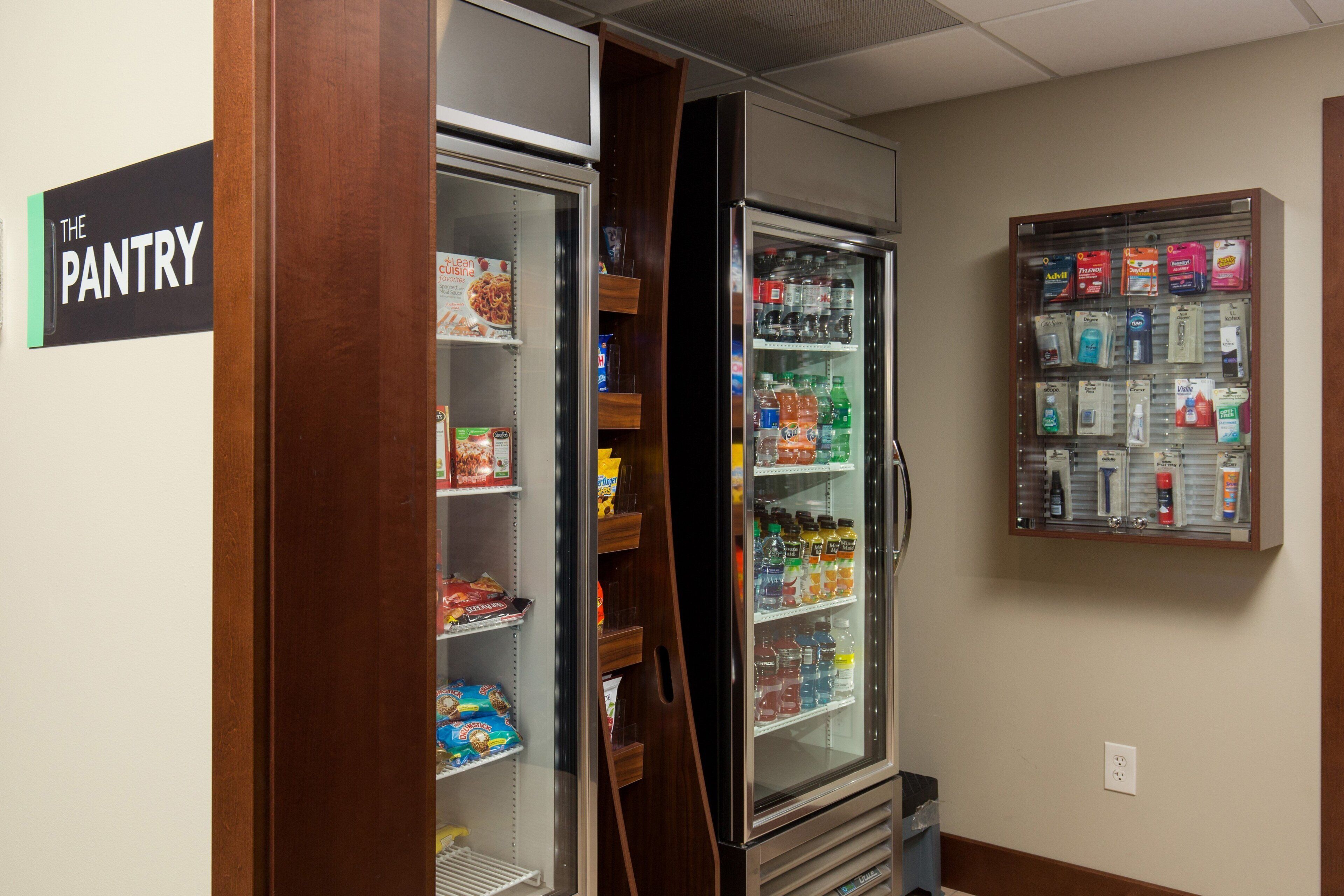 A pantry area with a refrigerator stocked with beverages and snacks, and a vending machine with various products.