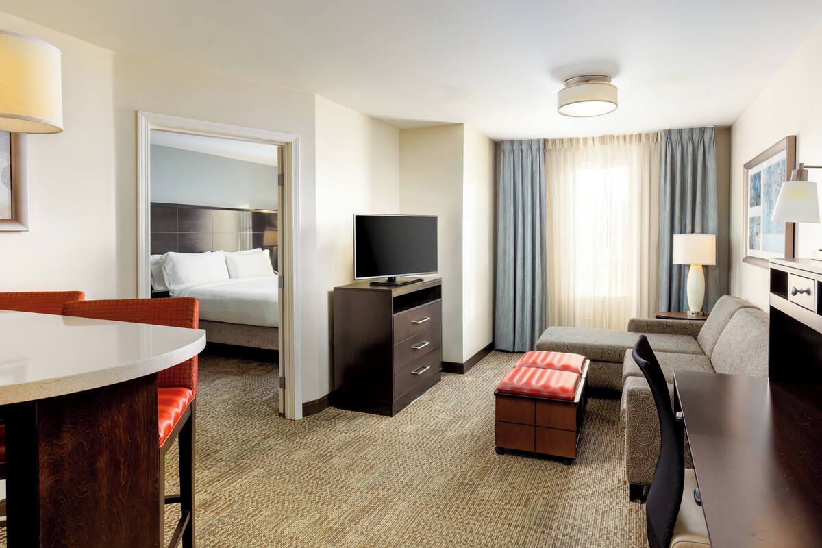 A hotel room with a bed, a desk, a chair, a television, and a sofa.