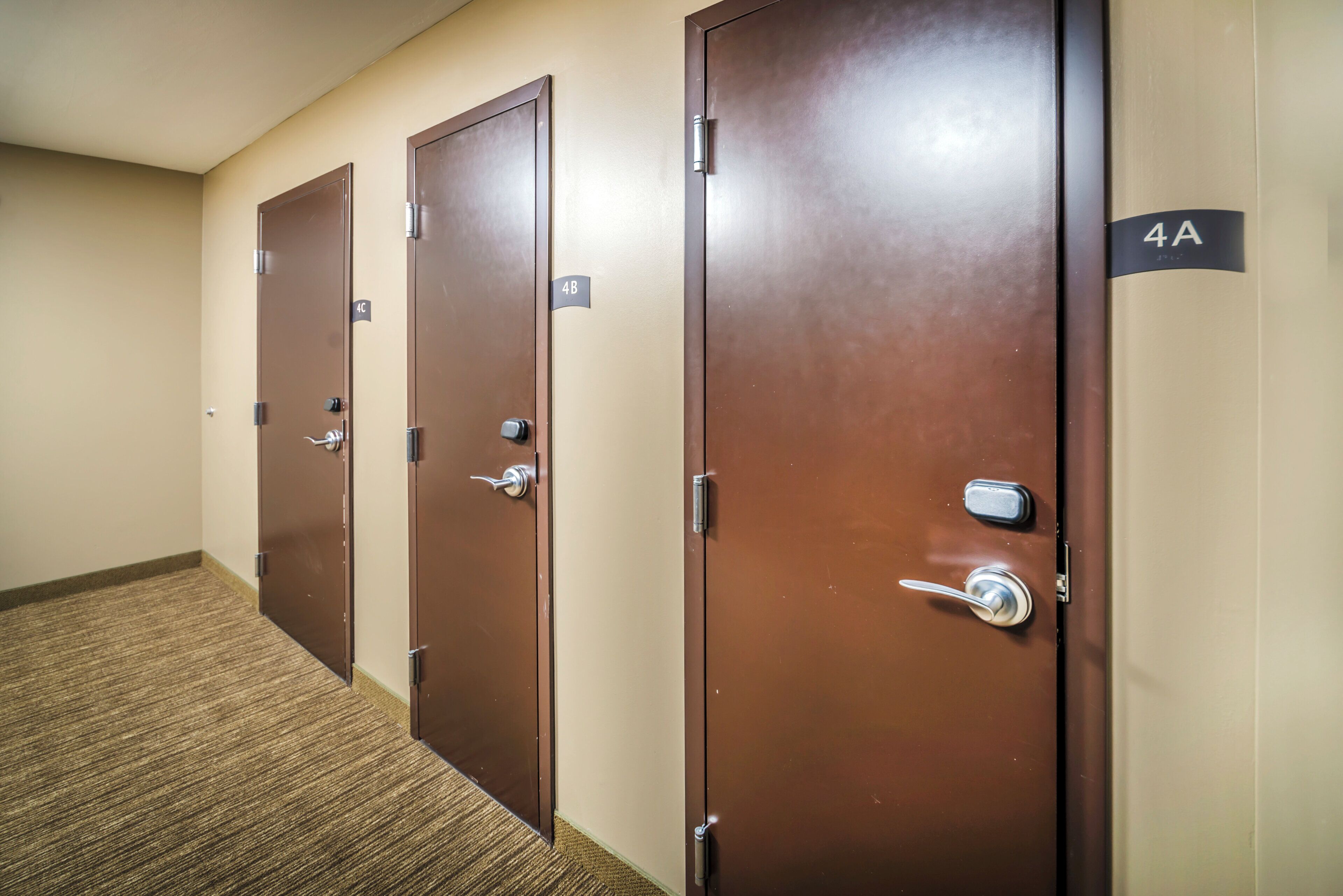 A row of brown doors with numbered signs, carpeted floor, and a plain wall.