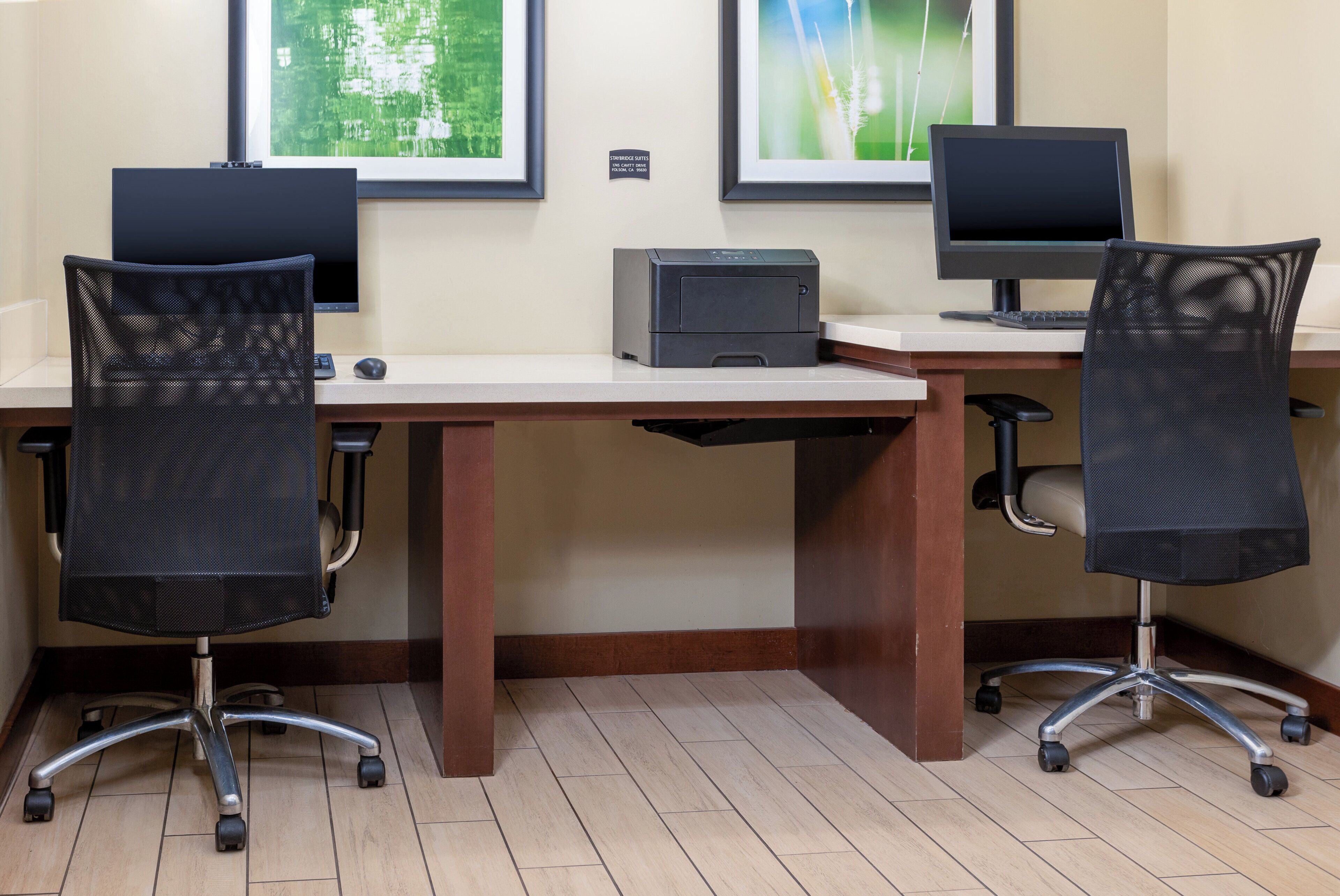 A workspace with two desks, each with a computer and a printer, and two mesh office chairs.