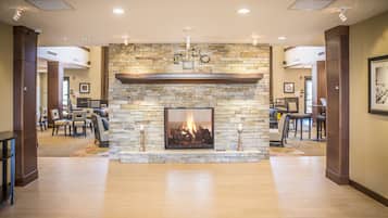 A spacious lobby with a stone fireplace, wooden flooring, and a dining area with tables and chairs.