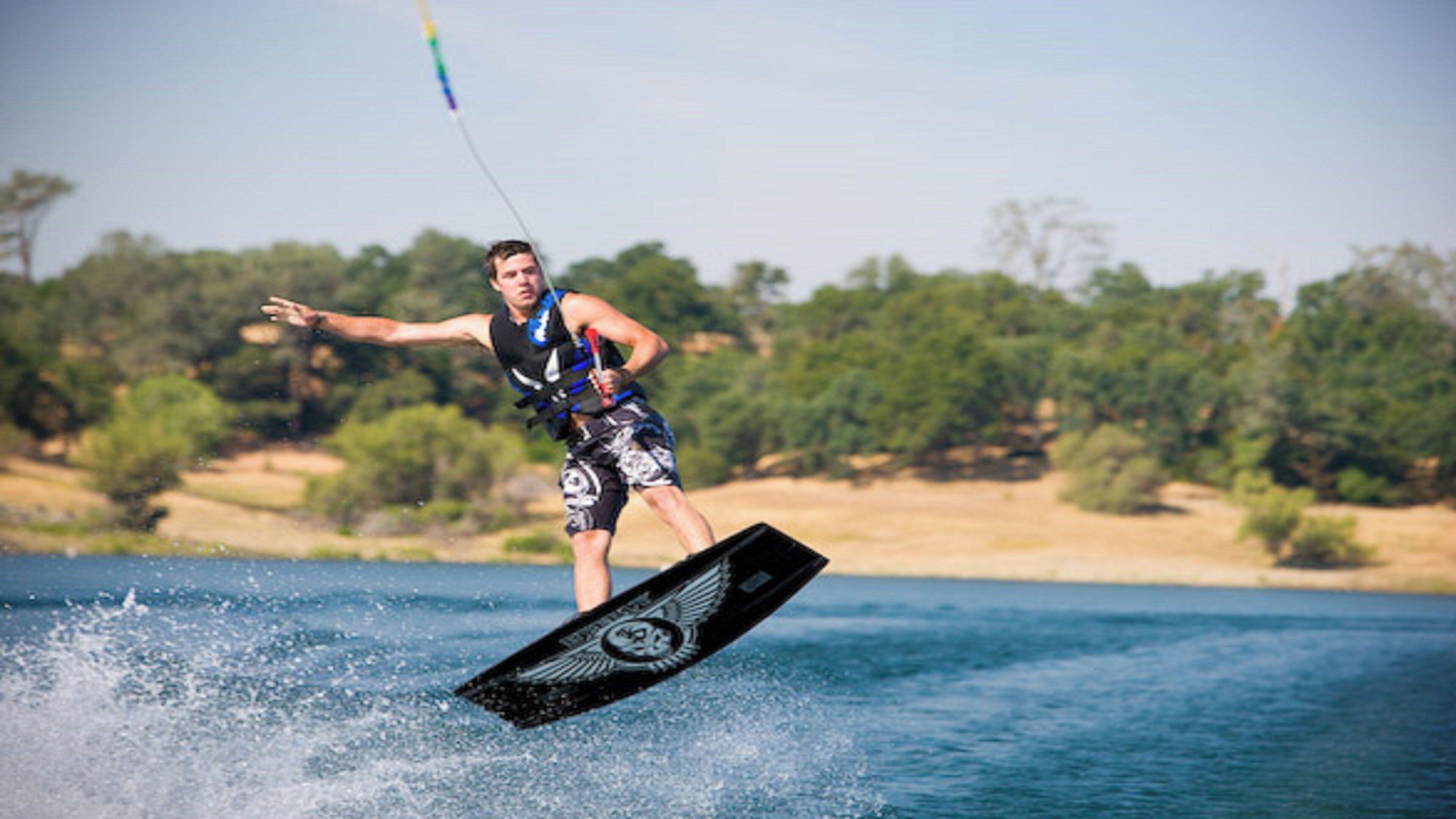 Uma pessoa praticando wakeboard em um corpo d'água, com árvores ao fundo.