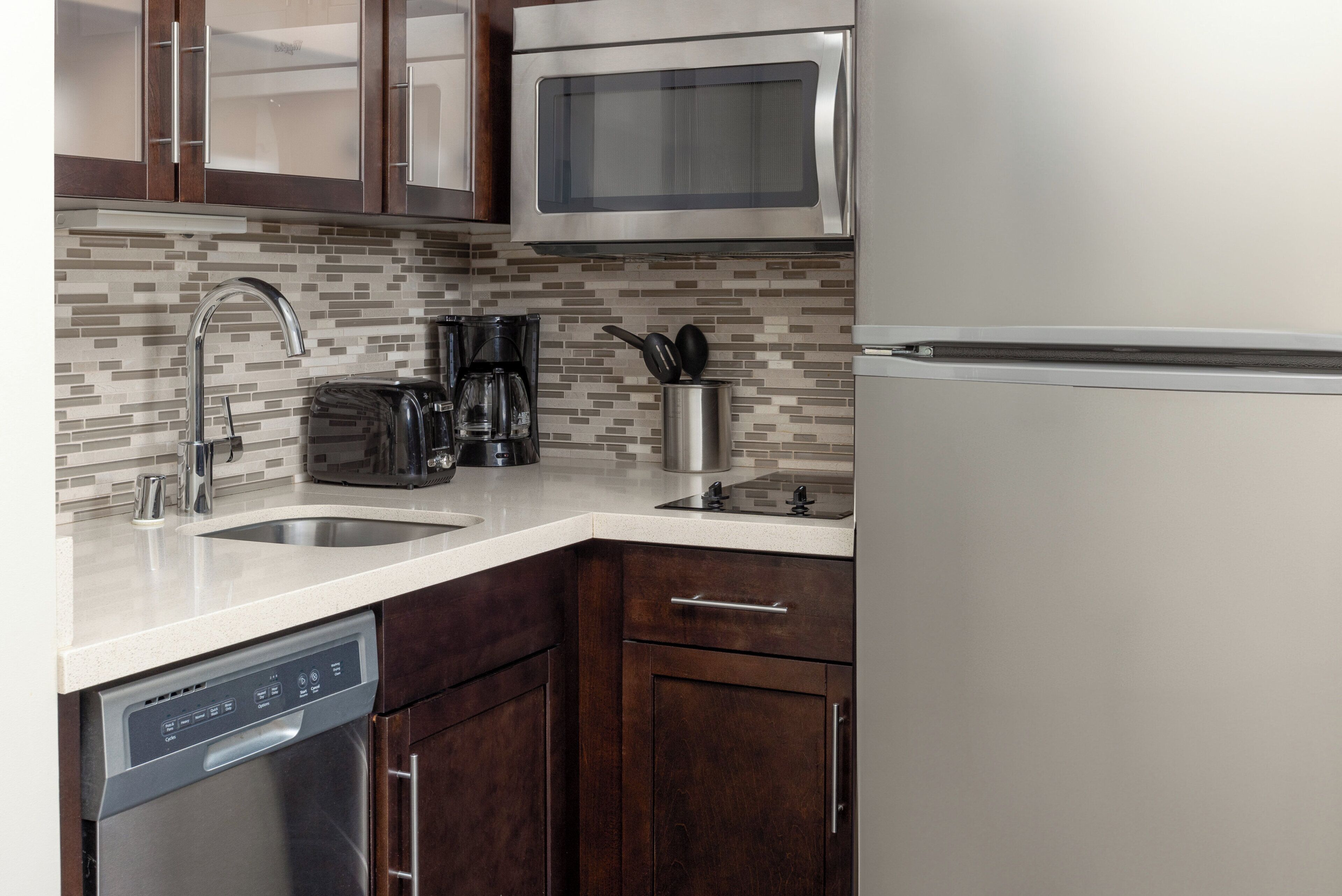 A kitchen with a dishwasher, coffee maker, microwave, and stainless steel refrigerator.