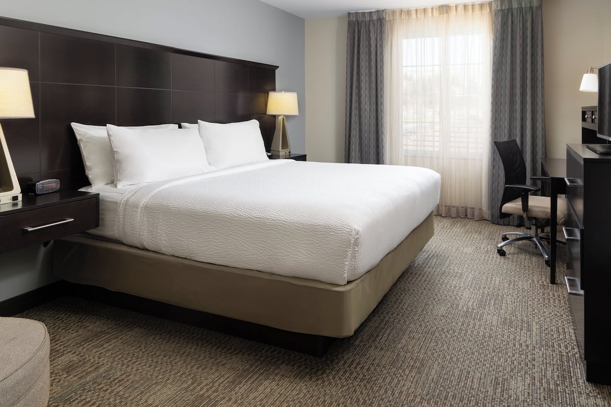 A hotel room with a large bed, two bedside tables with lamps, a desk with a chair, and a TV.