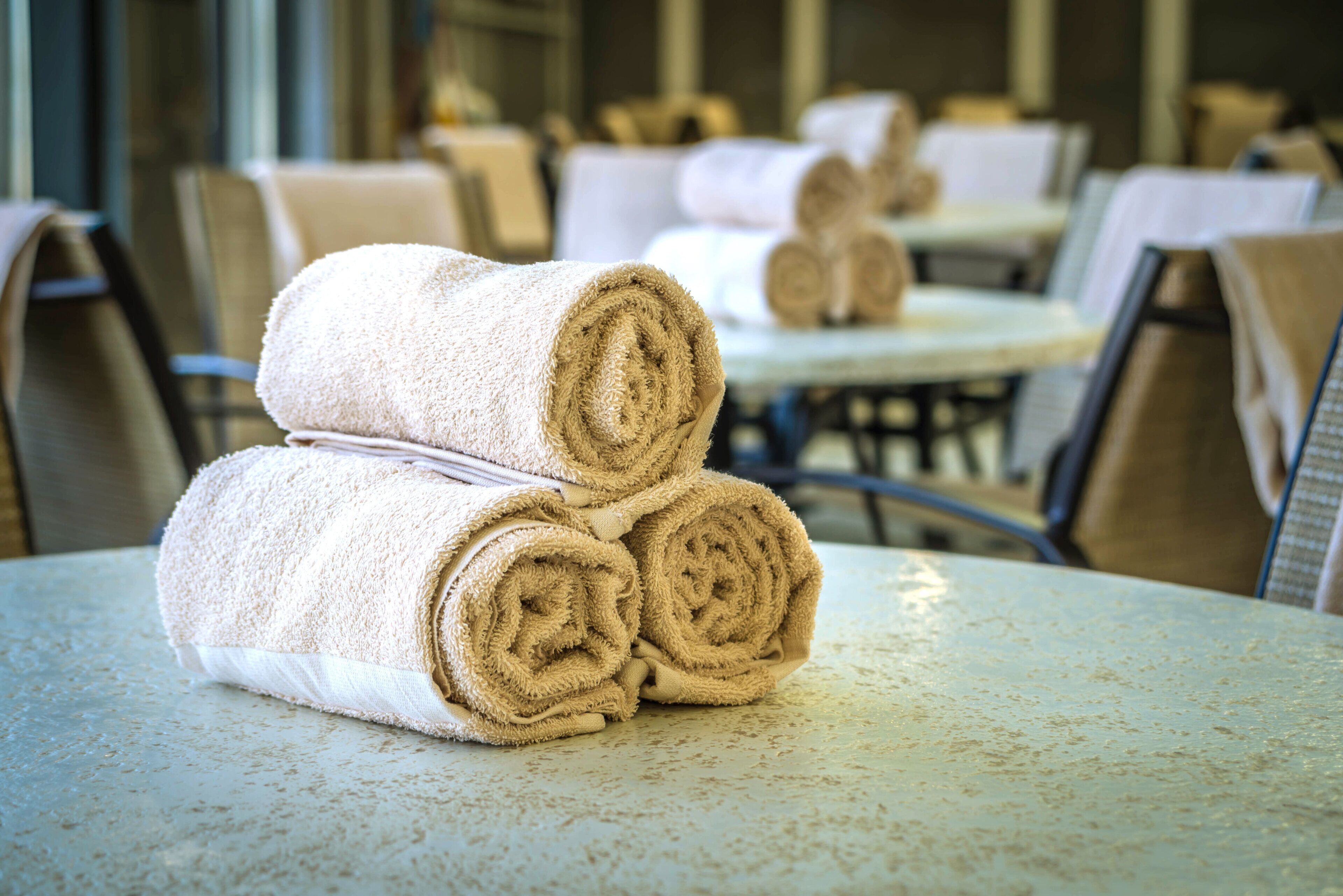 A table with rolled towels and a chair in a hotel room.