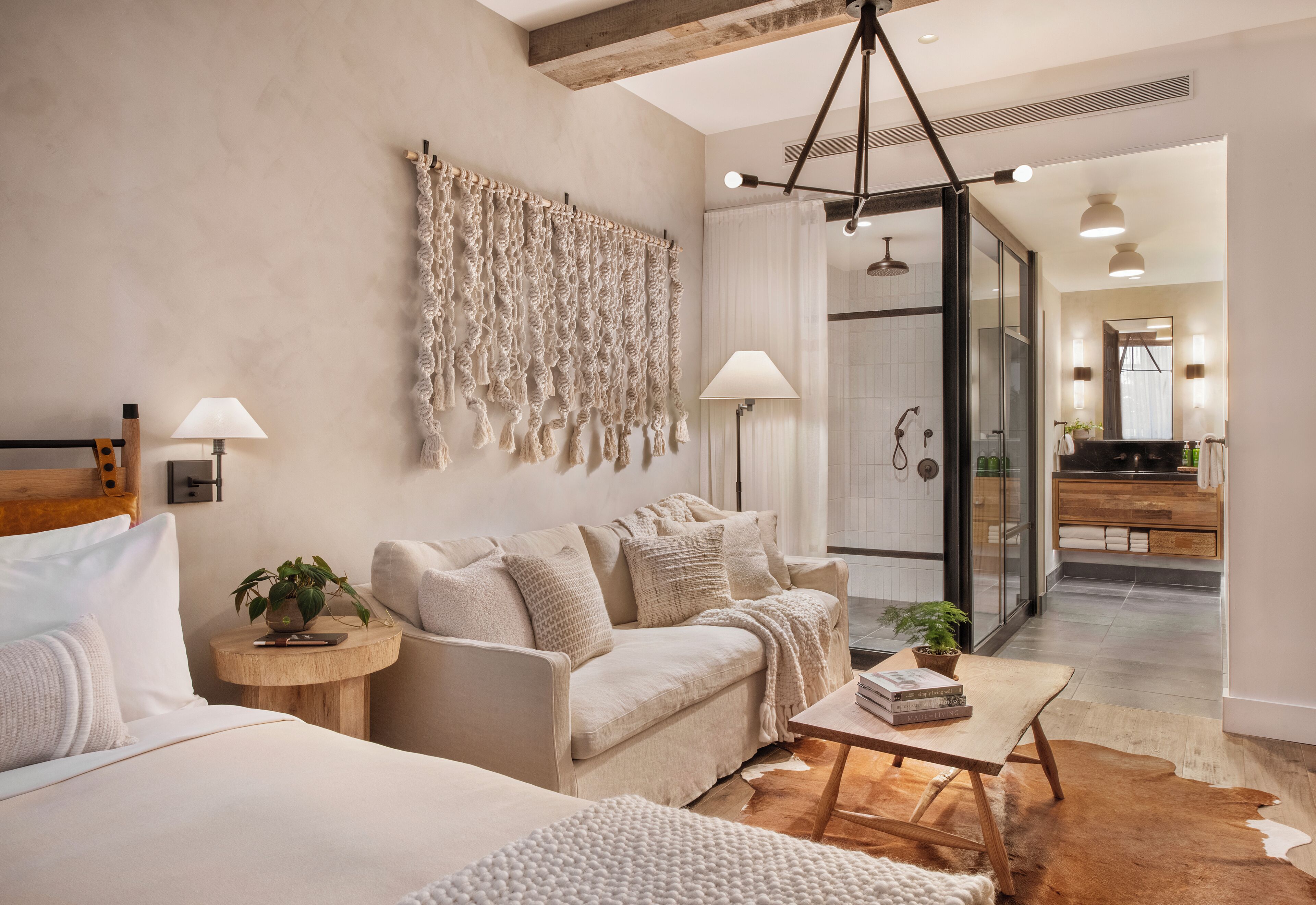A modern bedroom with a sofa, a bedside table with a lamp, a cowhide rug, and a wall-mounted macrame piece.