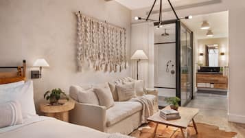 A modern bedroom with a sofa, a bedside table with a lamp, a cowhide rug, and a wall-mounted macrame piece.