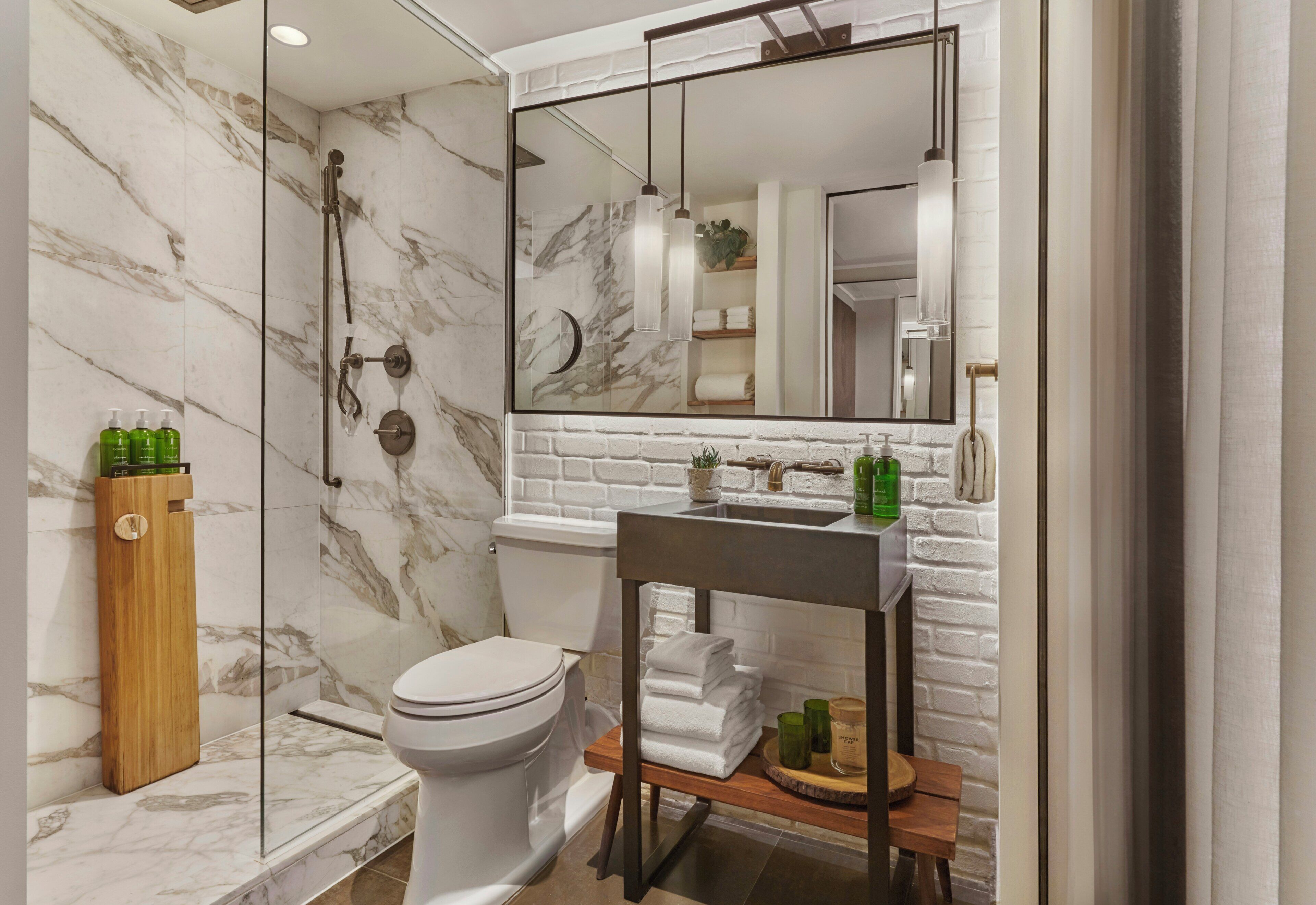 A bathroom with a marble wall, a glass shower enclosure, a white toilet, a wooden vanity, and a large mirror.