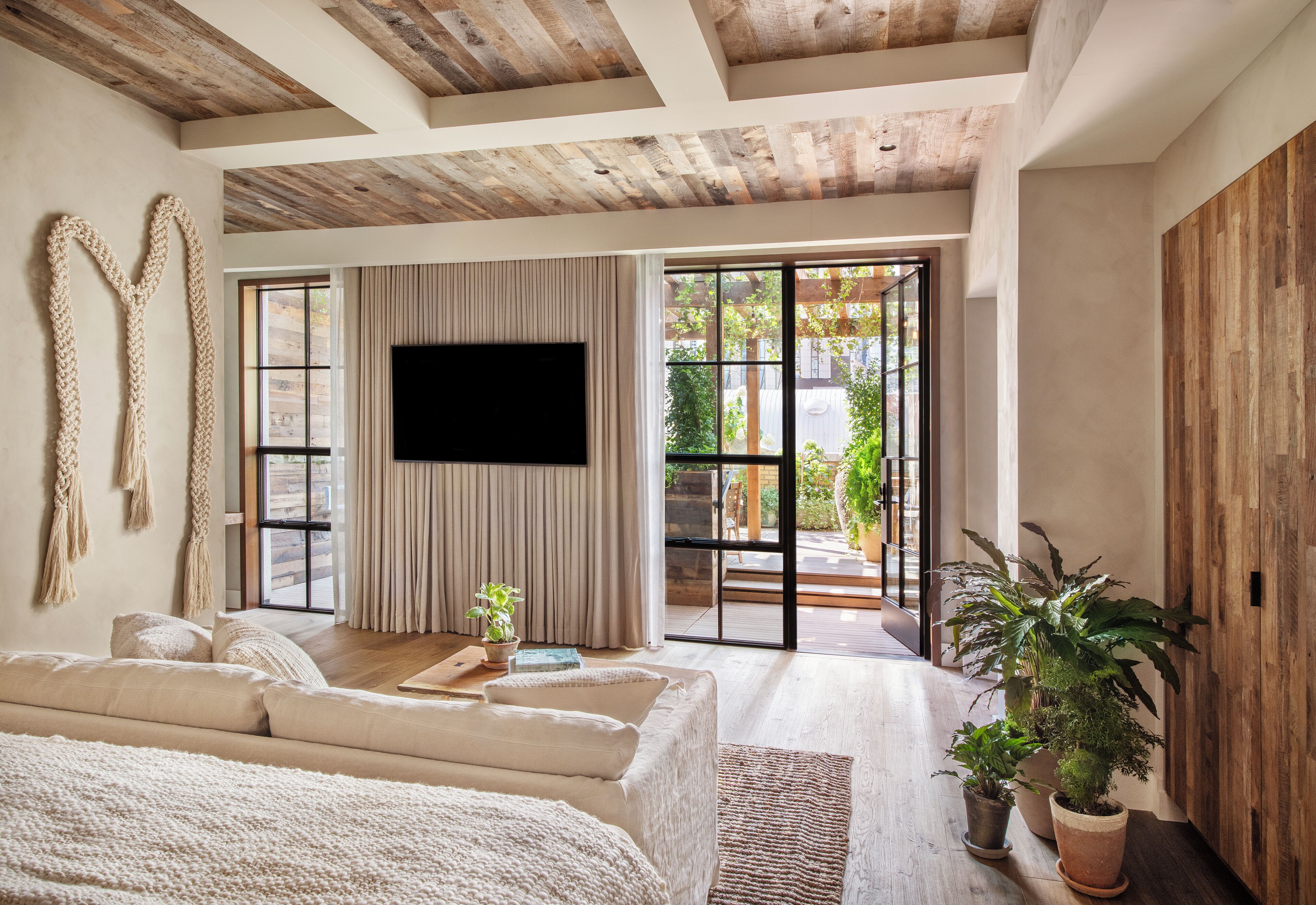 A spacious room with a large bed, a flat-screen TV, a sliding glass door leading to an outdoor area, and a wooden ceiling.