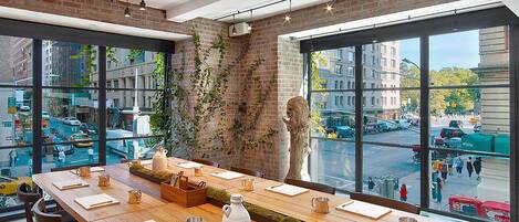A modern conference room with a long table, chairs, and a large window offering a city view.