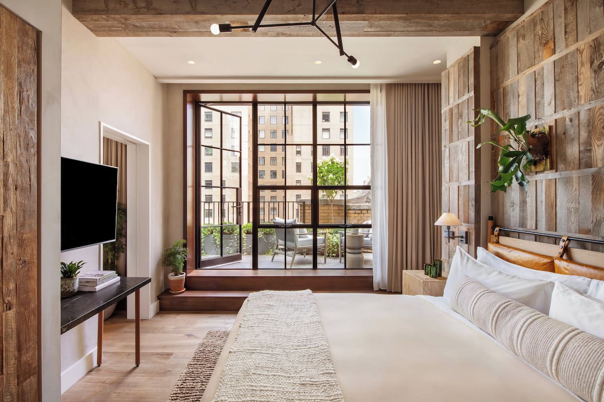 Quarto moderno com uma cama grande, uma TV e vista da cidade através de janelas do chão ao teto.