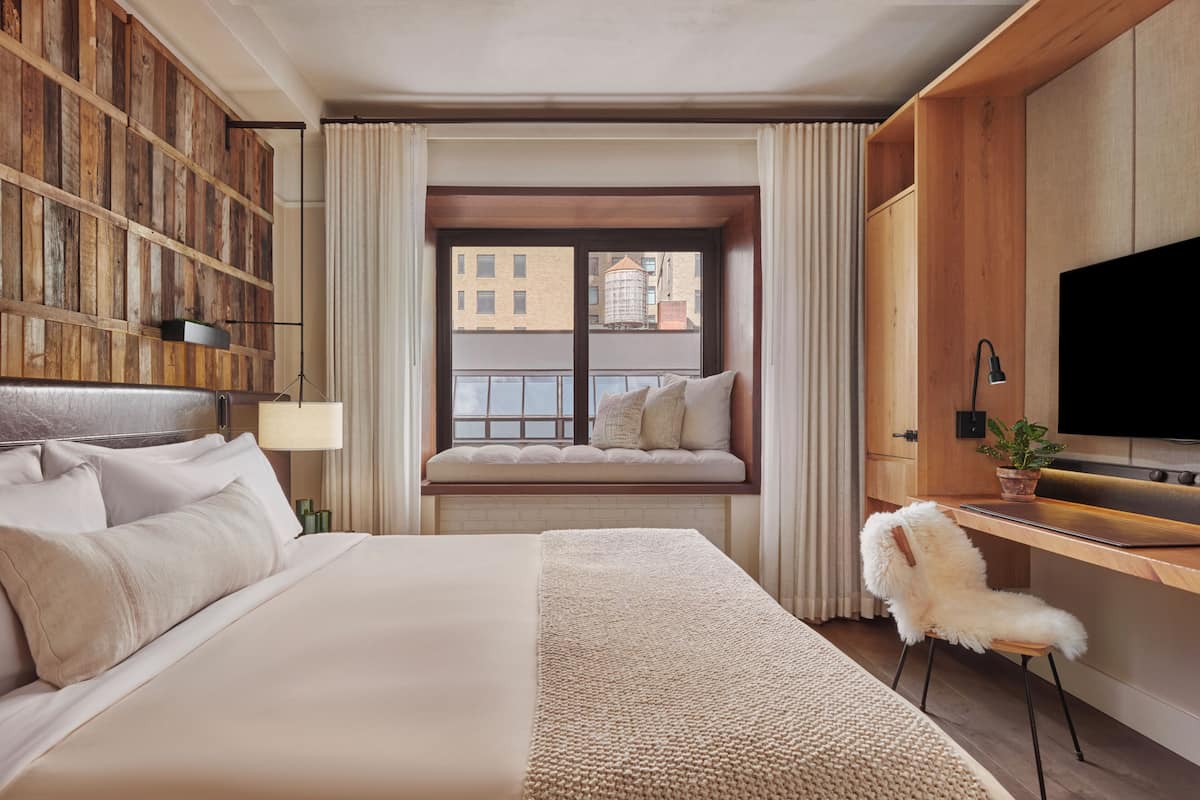 Quarto de hotel com cama grande, parede de madeira, um assento junto à janela, escrivaninha e televisão.