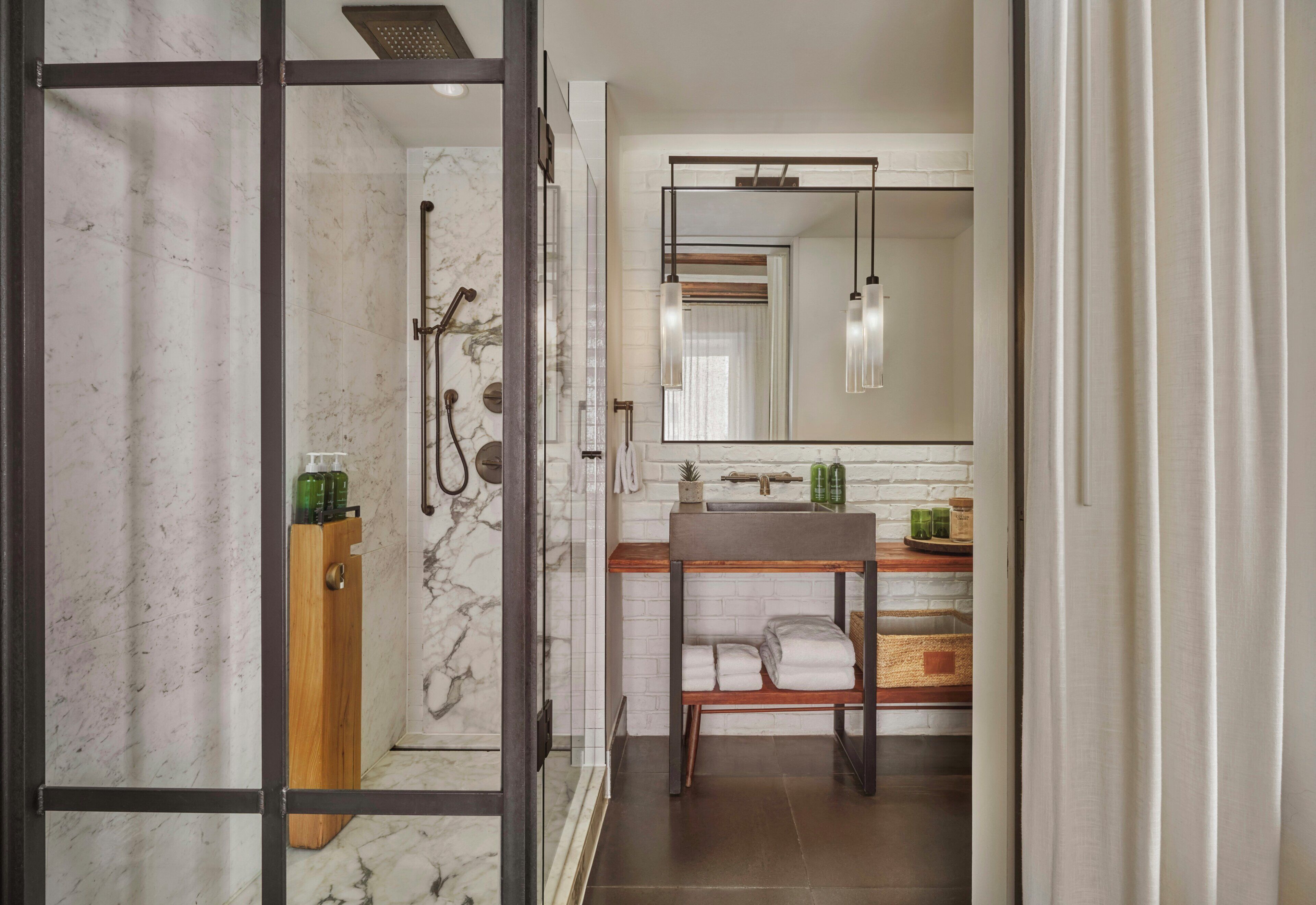 A bathroom with a shower, a sink, a mirror, and a wooden shelf with towels.