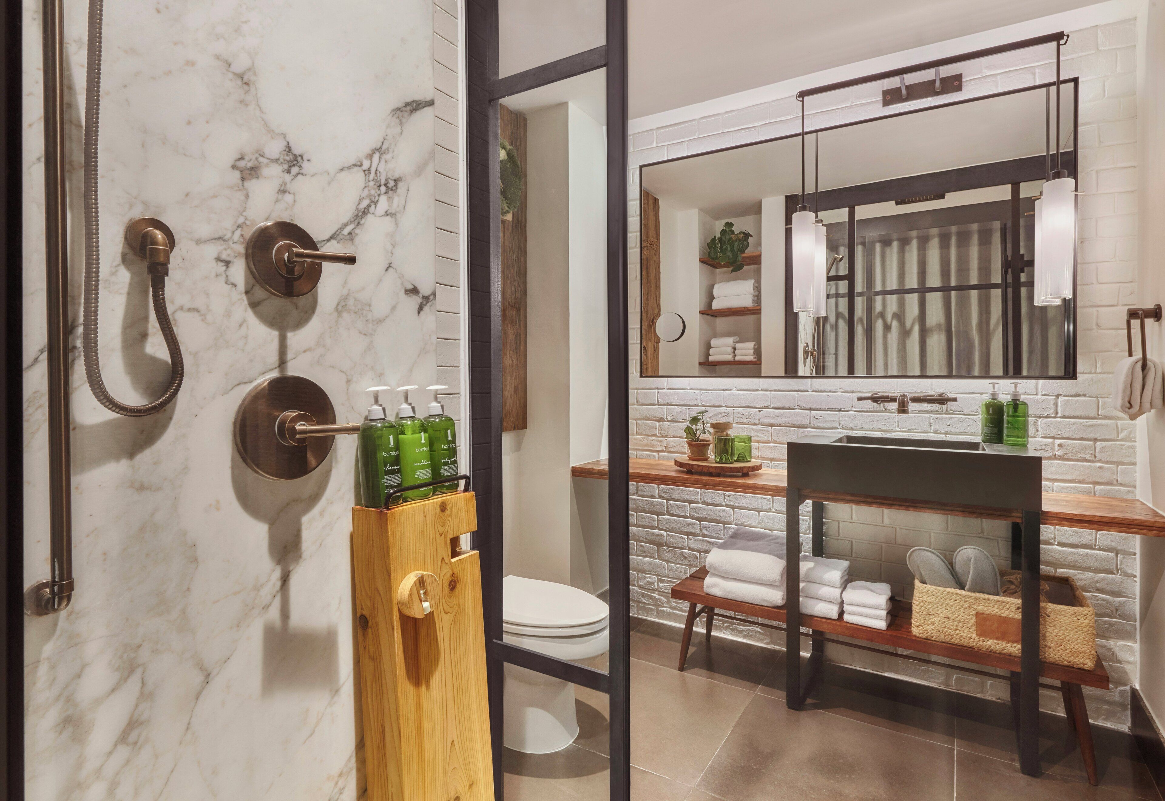 A bathroom with a marble wall, a wooden towel rack, a sink with a mirror above it, and a toilet.