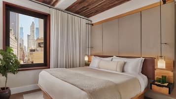 A hotel room with a large bed, a window with curtains, a potted plant, and a city view.