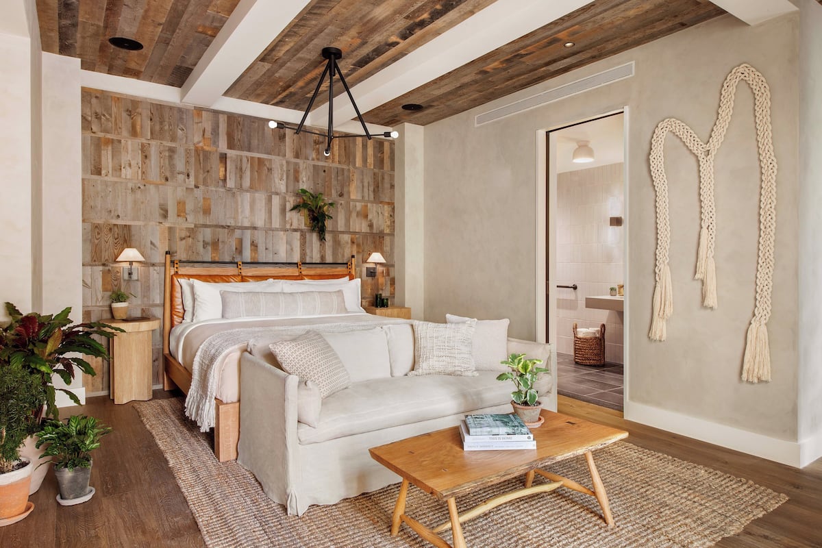 Quarto com teto de madeira, cama, sofá, mesa de centro e parede com detalhes em macramé.