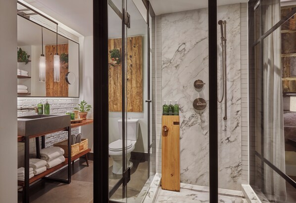 A modern bathroom with a glass shower enclosure, marble walls, a wooden vanity, and a large mirror. - 1 Hotel Central Park (New York)